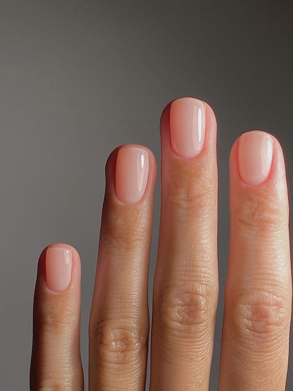 Macro close-up of a woman's hand showcasing a minimalist soap nails manicure with a high-shine glassy top coat over a sheer translucent milky pink nail polish.