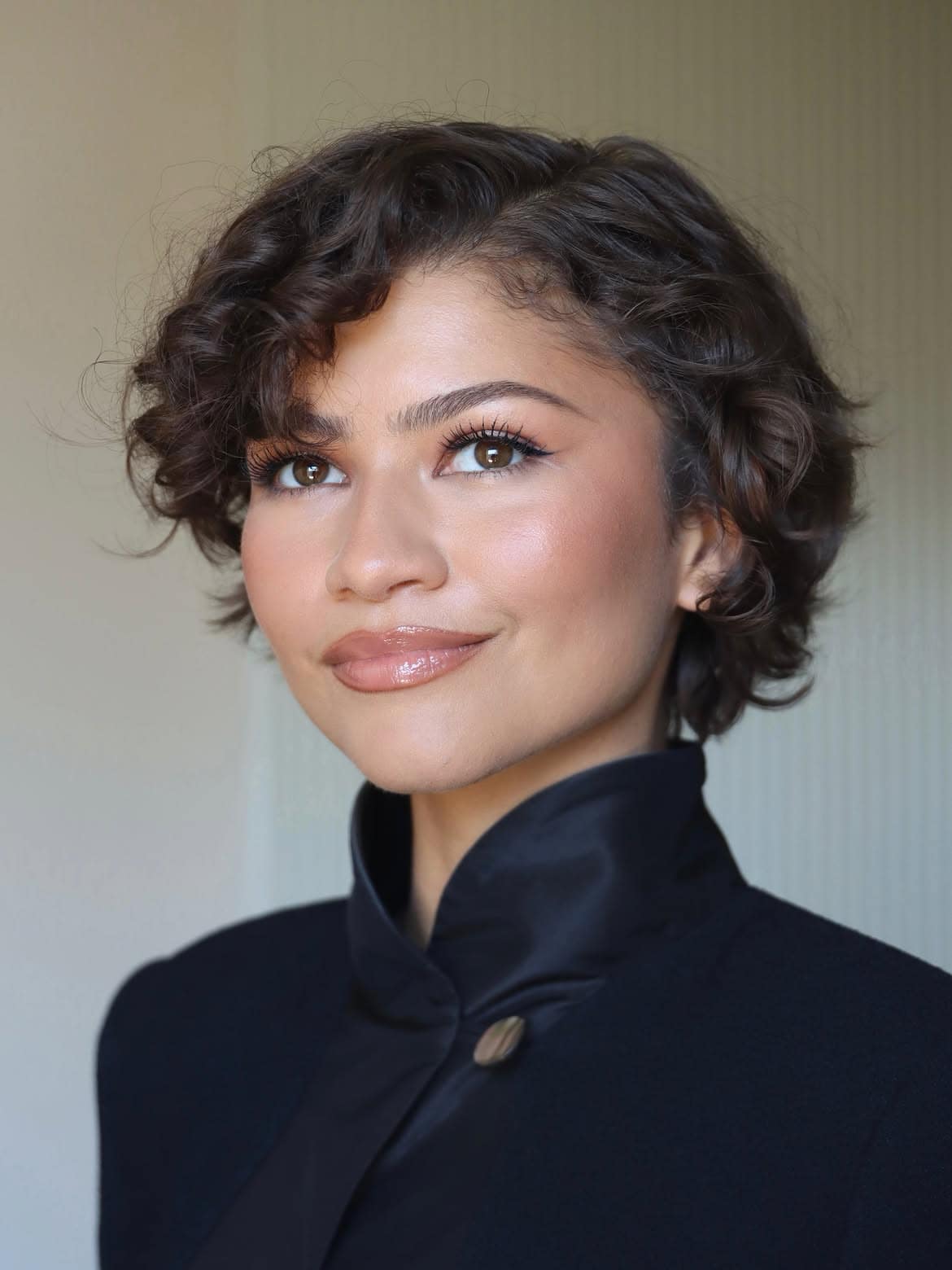 A close-up portrait of Zendaya showcasing the anti-blush makeup trend. Her cheekbones are defined with low-saturation, muted taupe tones instead of bright pinks, emphasizing a clean, minimalist bare skin aesthetic and a natural complexion.