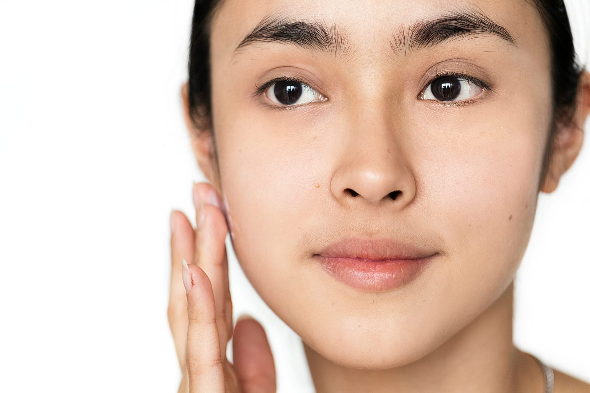 Close-up portrait of a woman gently pressing her fingertips against her cheek to test skin bounce and hydration during her morning skincare routine.