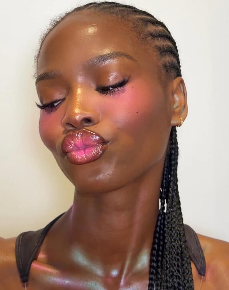 Close-up of a woman with dark skin and black hair showing the viral melted flush blush trend and a radiant highlight on her neck.