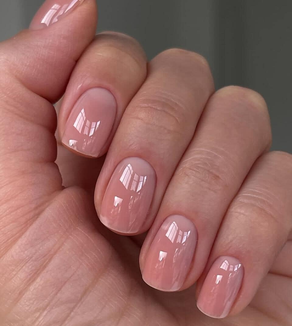 Close-up of a hand with a short glass manicure, ultra-glossy clear top coat, and clean natural nails.